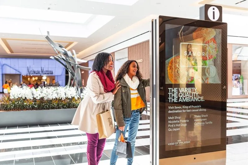 Shoppers walking past a digital advertising screen in a mall