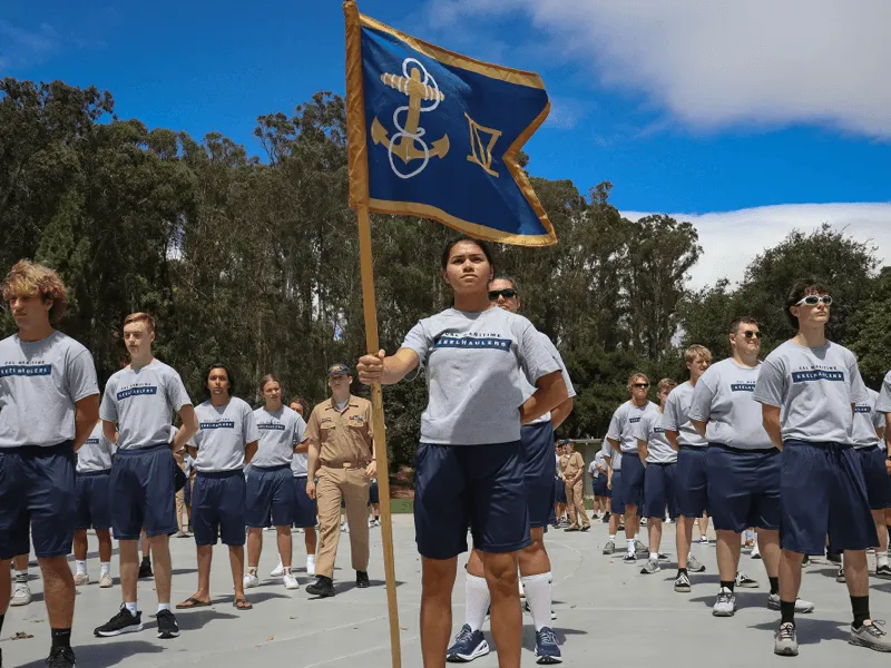 Cadets in uniform marching with a flag
